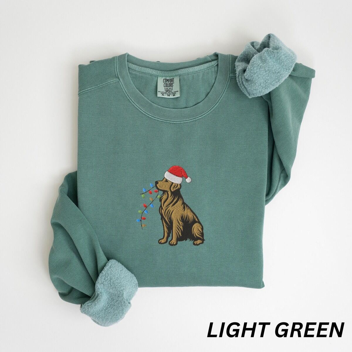 Festive Golden Retriever Sweatshirt – Light Green Festive golden retriever sweatshirt in Light Green laid flat with rolled cuffs, embroidered with a golden in a Santa hat holding Christmas lights