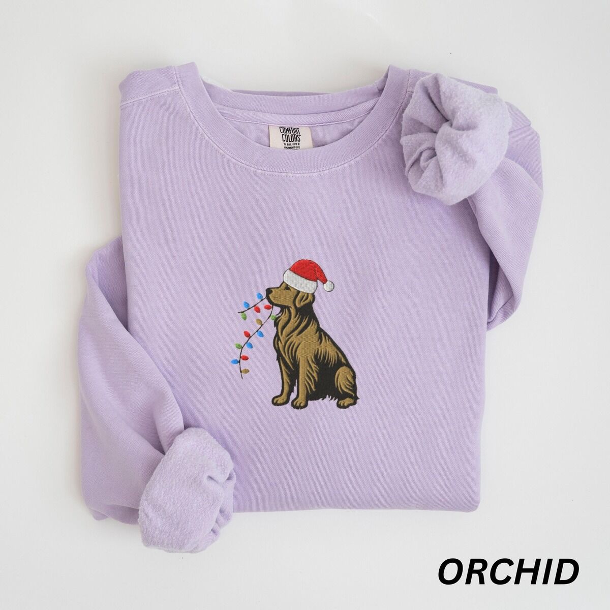 Festive Golden Retriever Sweatshirt – Orchid Orchid crewneck sweatshirt laid flat, embroidered with a golden retriever in a red Santa hat holding Christmas lights