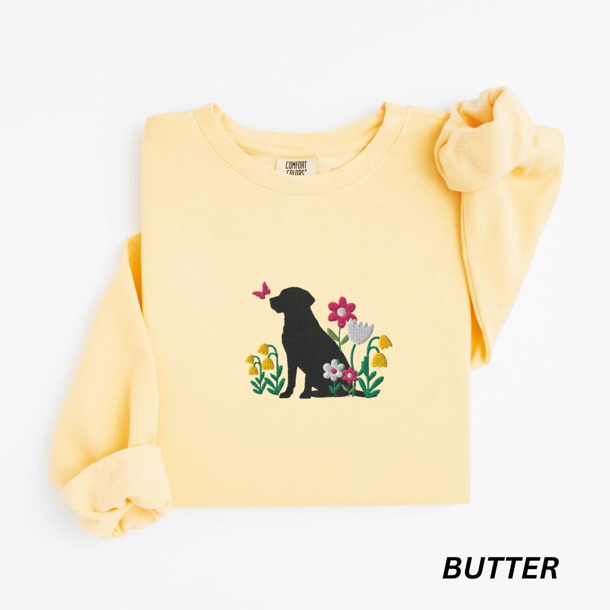 Floral Black Lab Sweatshirt – Butter Butter crewneck sweatshirt laid flat on white, embroidered with a sitting black Labrador silhouette among yellow bell flowers, a white tulip and pink daisies, with a pink butterfly