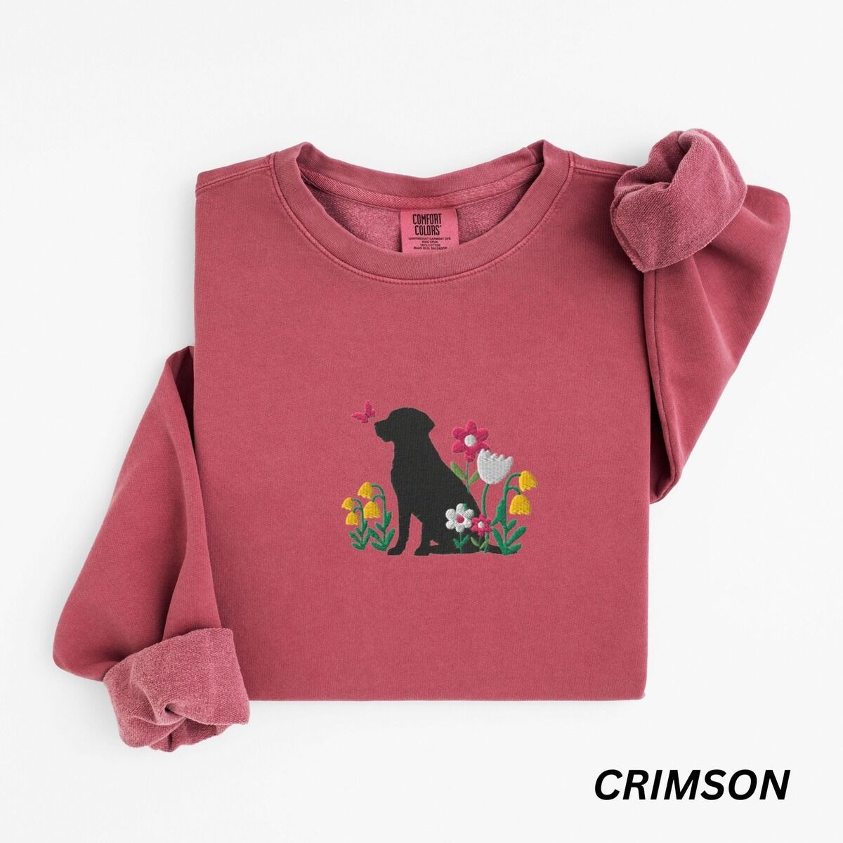 Floral Black Lab Sweatshirt – Crimson Crimson crewneck sweatshirt laid flat on white, embroidered with a sitting black Labrador silhouette among yellow bell flowers, a white tulip and pink daisies, with a pink butterfly