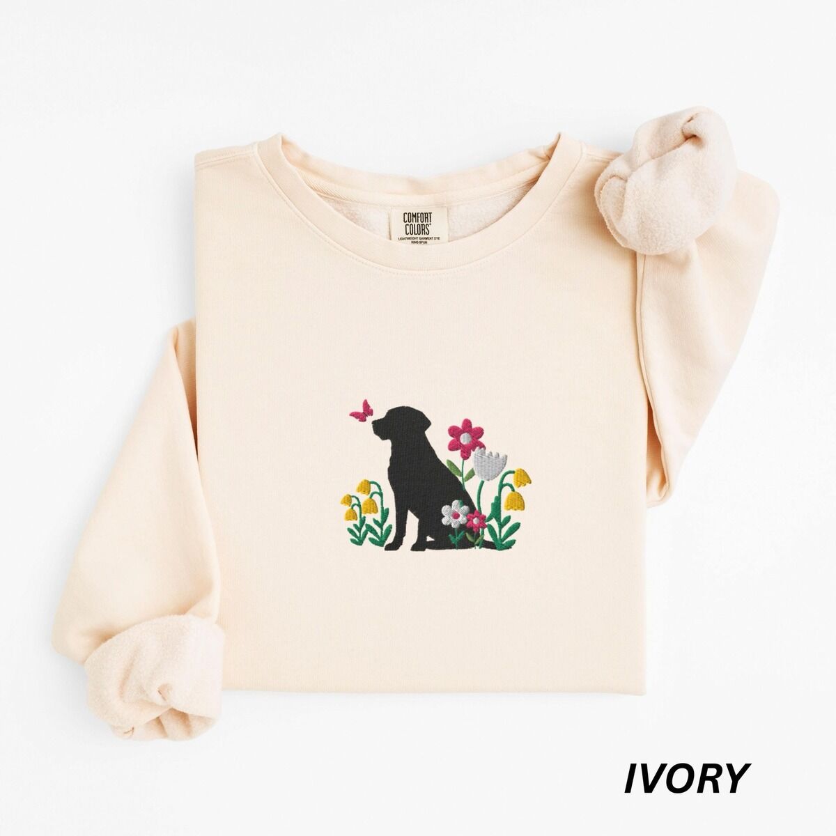 Floral Black Lab Sweatshirt – Ivory Ivory crewneck sweatshirt laid flat on white, embroidered with a sitting black Labrador silhouette among yellow bell flowers, a white tulip and pink daisies, with a pink butterfly