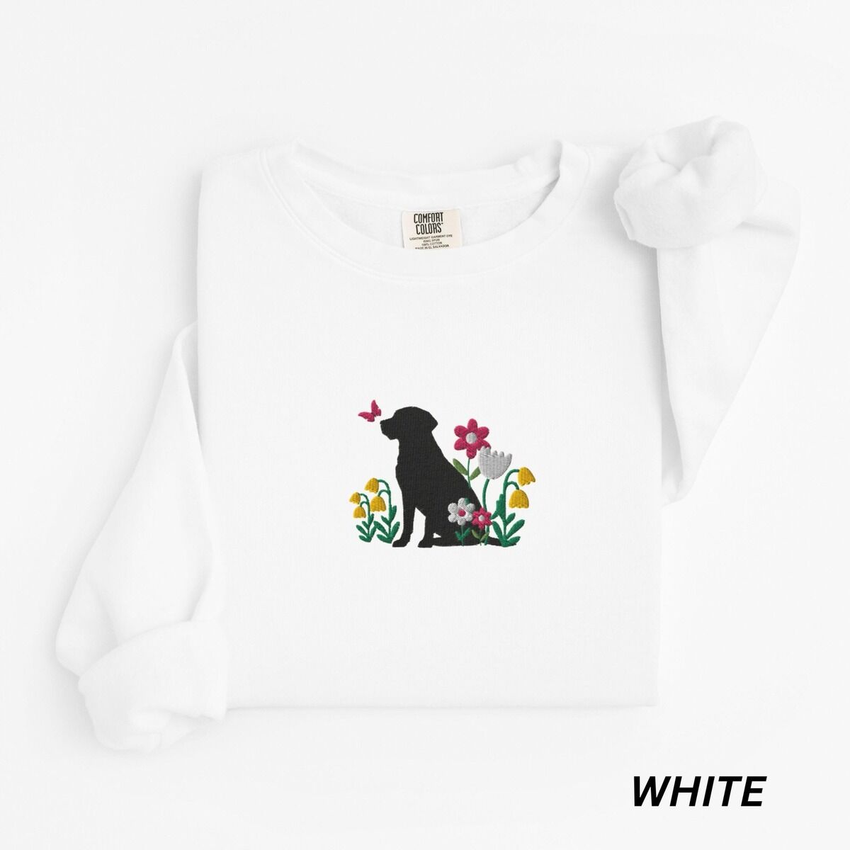 Floral Black Lab Sweatshirt – White White crewneck sweatshirt laid flat on white, embroidered with a sitting black Labrador silhouette among yellow bell flowers, a white tulip and pink daisies, with a pink butterfly