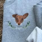 Embroidered brown and white dog portrait with an olive branch wreath and the name Kaydo in white script on a sport grey sweatshirt