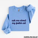 Carolina Blue crewneck sweatshirt folded on a white background, with the words ask me about my foster cat embroidered in cursive across the chest in navy thread