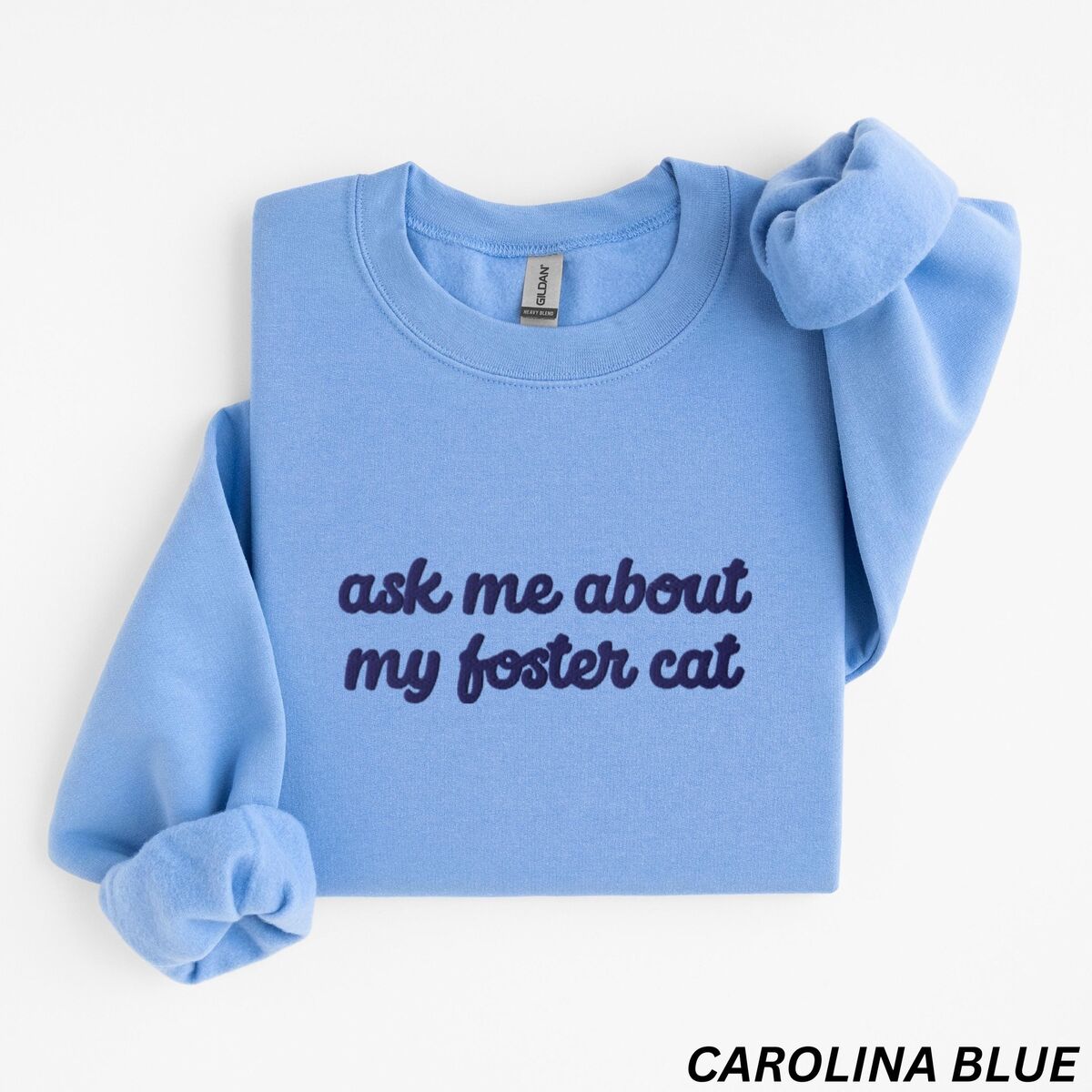 Foster Cat Sweatshirt Carolina Blue Carolina Blue crewneck sweatshirt folded on a white background, with the words ask me about my foster cat embroidered in cursive across the chest in navy thread