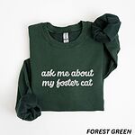 Forest Green crewneck sweatshirt folded on a white background, with the words ask me about my foster cat embroidered in cursive across the chest in light gray thread
