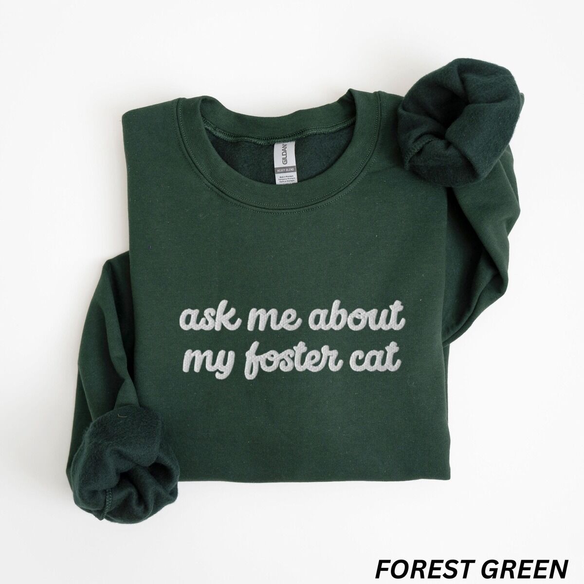 Foster Cat Sweatshirt – Forest Green Forest Green crewneck sweatshirt folded on a white background, with the words ask me about my foster cat embroidered in cursive across the chest in light gray thread