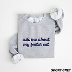 Sport Grey crewneck sweatshirt folded on a white background, with the words ask me about my foster cat embroidered in cursive across the chest in navy thread