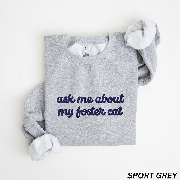 Sport Grey crewneck sweatshirt folded on a white background, with the words ask me about my foster cat embroidered in cursive across the chest in navy thread