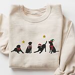 Sand crewneck sweatshirt laid flat with rolled cuffs, embroidered with four black Labrador silhouettes in a bow, a candy-cane scarf, a Santa hat and an elf hat under gold stars