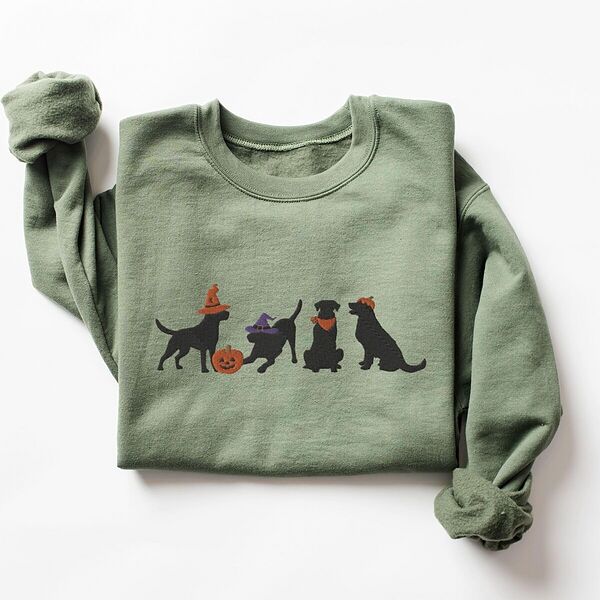 Military Green crewneck sweatshirt laid flat on a white background, embroidered with four black lab silhouettes in a row, two in witch hats, one in a bandana and one with a tiny pumpkin hat, beside a jack-o'-lantern