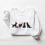 White crewneck sweatshirt laid flat on a white background, embroidered with four black lab silhouettes in a row, two in witch hats, one in a bandana and one with a tiny pumpkin hat, beside a jack-o'-lantern