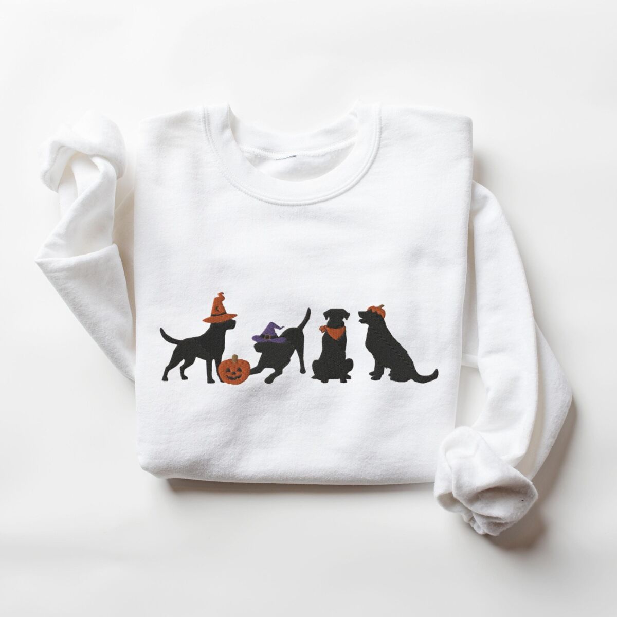 Four Black Labs Halloween Sweatshirt - White White crewneck sweatshirt laid flat on a white background, embroidered with four black lab silhouettes in a row, two in witch hats, one in a bandana and one with a tiny pumpkin hat, beside a jack-o'-lantern