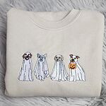 Sand crewneck sweatshirt folded on a gray faux fur rug, embroidered with four dogs in white ghost sheets standing in a row, the last one holding a jack-o'-lantern bucket