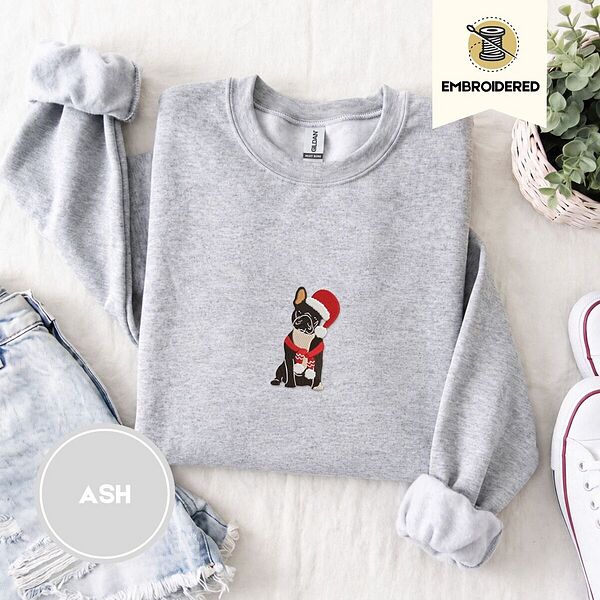Ash crewneck sweatshirt folded with denim shorts, white sneakers and a potted plant, embroidered with a black French bulldog with a cream chest in a Santa hat and a red scarf with white zigzag stripes