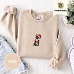 Sand crewneck sweatshirt folded with denim shorts, white sneakers and a potted plant, embroidered with a black French bulldog with a cream chest in a Santa hat and a red scarf with white zigzag stripes