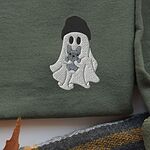 Close-up of the ghost and Frenchie embroidery stitched with a black beanie and a blue-grey French bulldog on a green sweatshirt, showing custom thread colors