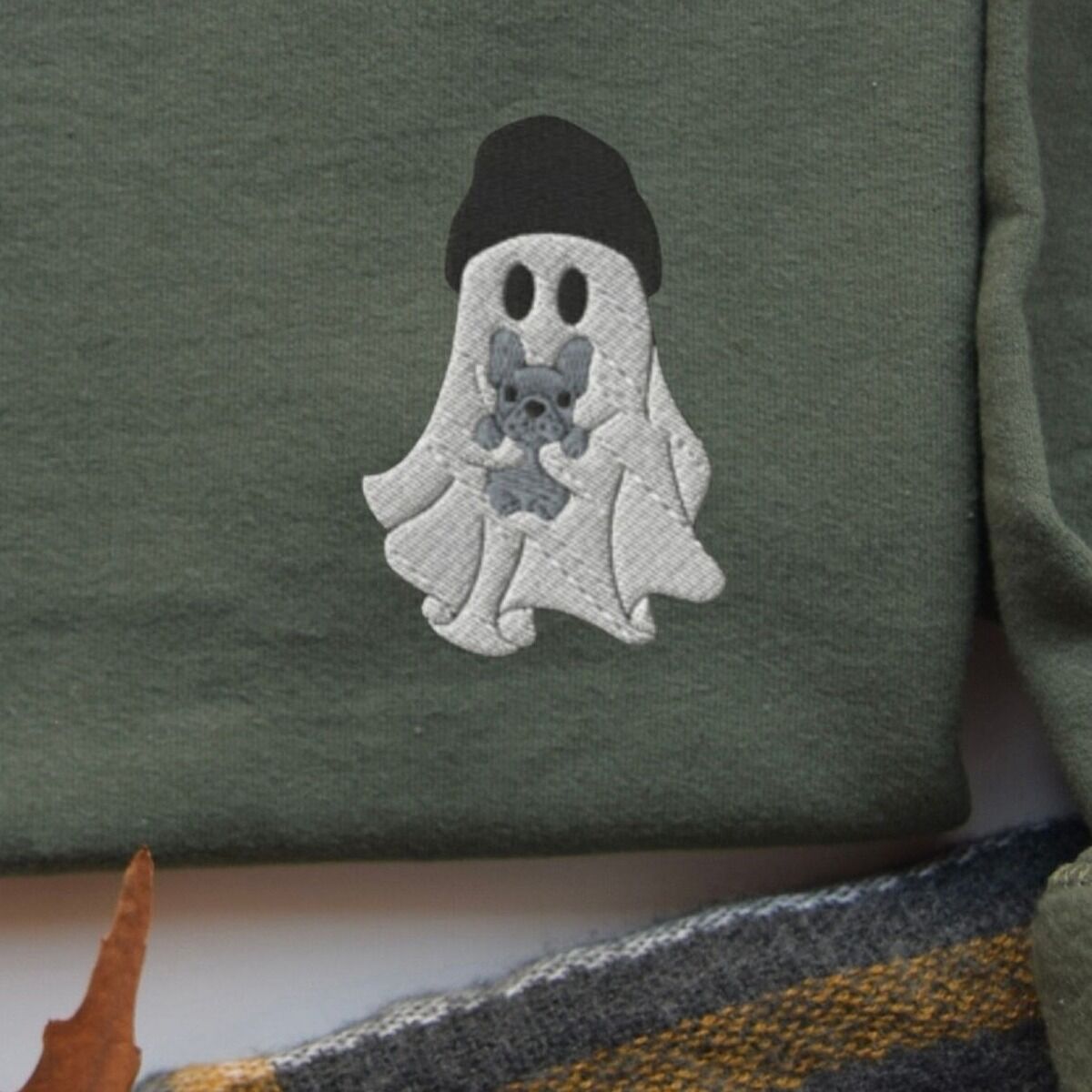 Frenchie Ghost Sweatshirt - custom colors Close-up of the ghost and Frenchie embroidery stitched with a black beanie and a blue-grey French bulldog on a green sweatshirt, showing custom thread colors