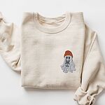 Sand crewneck sweatshirt laid flat on a white background, embroidered with a little ghost in a rust knit beanie hugging a grey French bulldog on the left chest
