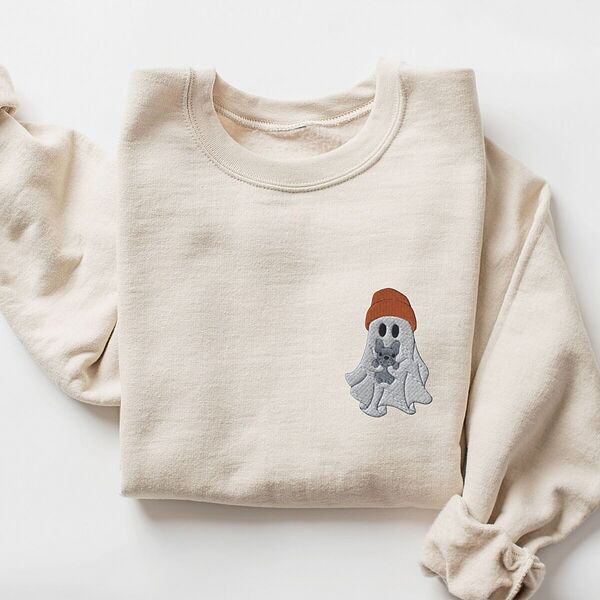 Sand crewneck sweatshirt laid flat on a white background, embroidered with a little ghost in a rust knit beanie hugging a grey French bulldog on the left chest