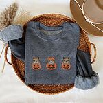 Dark Heather crewneck sweatshirt folded in a wicker basket with a felt hat and dried grass, embroidered with three fawn French bulldogs peeking out of carved jack-o'-lanterns