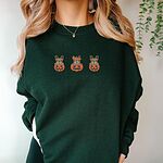 Woman wearing a Forest Green crewneck sweatshirt, embroidered with three fawn French bulldogs peeking out of carved jack-o'-lanterns