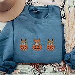 Indigo Blue crewneck sweatshirt laid flat on a printed backdrop with a felt hat and pampas grass, embroidered with three fawn French bulldogs peeking out of carved jack-o'-lanterns