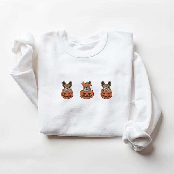 White crewneck sweatshirt laid flat on a white background, embroidered with three fawn French bulldogs peeking out of carved jack-o'-lanterns