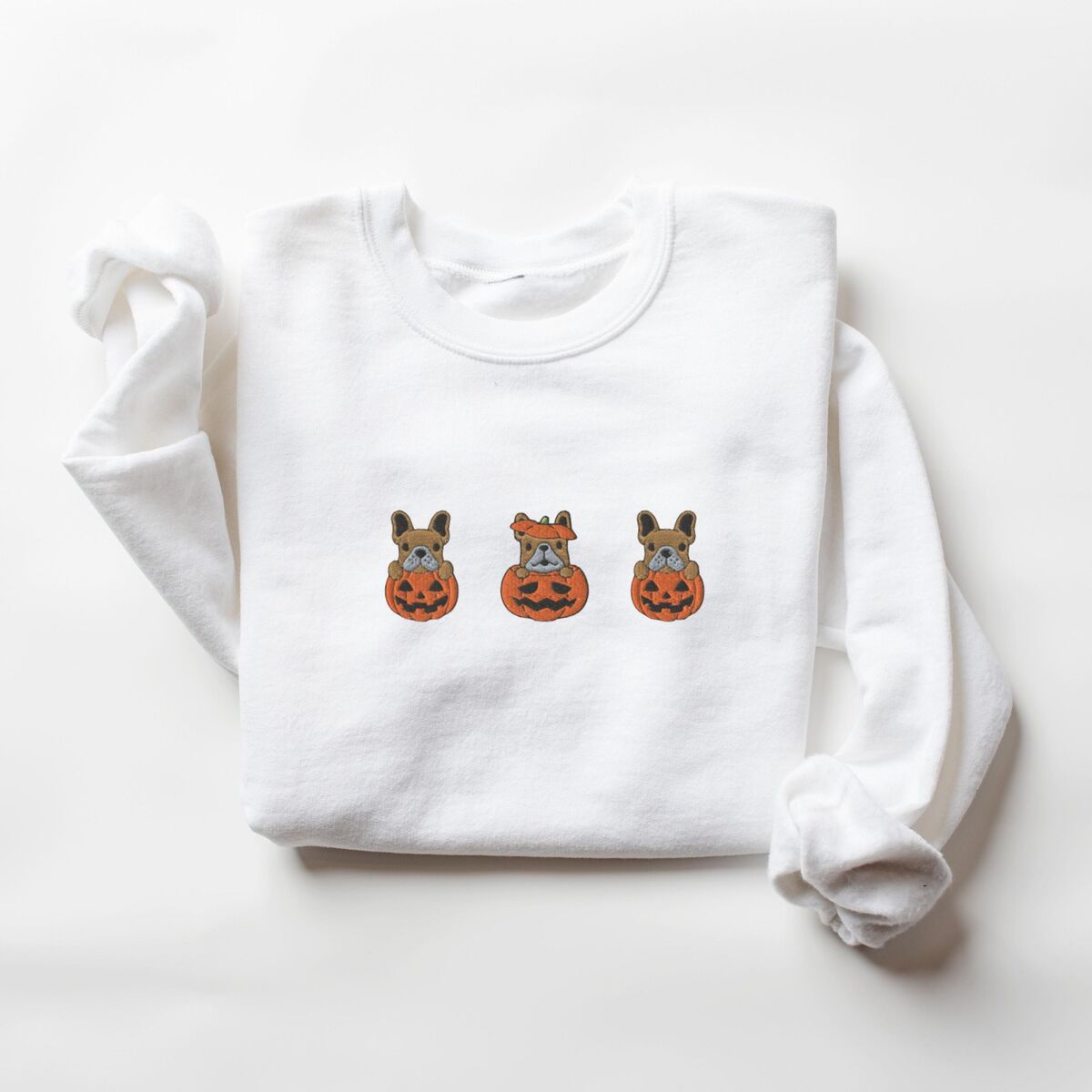 Frenchie Pumpkin Sweatshirt - White White crewneck sweatshirt laid flat on a white background, embroidered with three fawn French bulldogs peeking out of carved jack-o'-lanterns