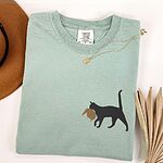 Bay Comfort Colors T-shirt embroidered with a black cat walking off with a golden toupee in its mouth on the left chest