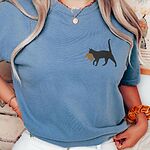 Blue Jean Comfort Colors T-shirt embroidered with a black cat walking off with a golden toupee in its mouth on the left chest
