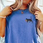 Flo Blue Comfort Colors T-shirt embroidered with a black cat walking off with a golden toupee in its mouth on the left chest