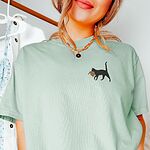 Island Reef Comfort Colors T-shirt embroidered with a black cat walking off with a golden toupee in its mouth on the left chest