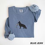 Blue Jean crewneck sweatshirt laid flat with a rolled cuff, embroidered with a black German shepherd silhouette carrying a string of colored Christmas lights