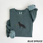 Blue Spruce crewneck sweatshirt laid flat with a rolled cuff, embroidered with a black German shepherd silhouette carrying a string of colored Christmas lights