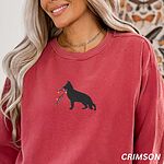 Smiling woman in a Crimson crewneck sweatshirt and silver necklace, embroidered with a black German shepherd silhouette carrying a string of colored Christmas lights