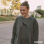 Woman outdoors on a street in a Pepper crewneck sweatshirt embroidered with a black German shepherd silhouette carrying a string of colored Christmas lights