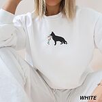 Woman in a White crewneck sweatshirt and matching sweatpants, embroidered with a black German shepherd silhouette carrying a string of colored Christmas lights