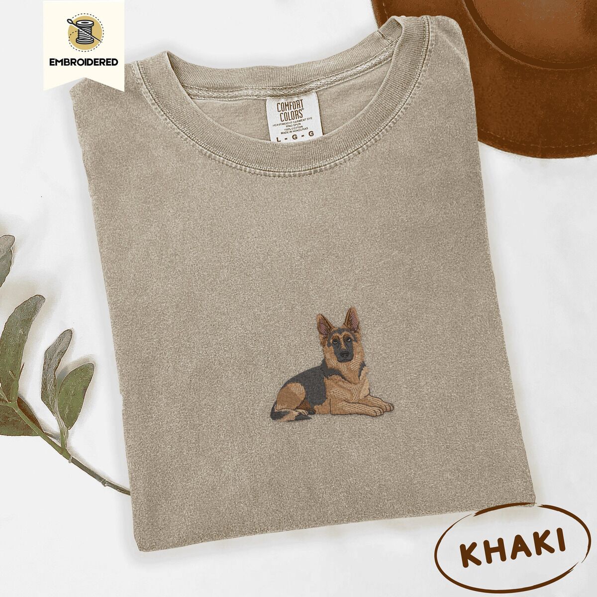 German Shepherd Shirt – Khaki Khaki Comfort Colors T-shirt embroidered with a black and tan German shepherd lying down with its ears up and its paws forward