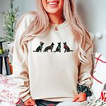 Smiling woman in a Sand crewneck sweatshirt embroidered with four black German shepherd silhouettes in a Santa hat, striped scarves and a red bow