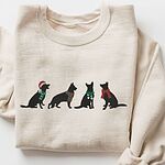 Sand crewneck sweatshirt laid flat, embroidered with four black German shepherd silhouettes in a Santa hat, striped scarves and a red bow