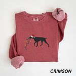 Crimson crewneck sweatshirt laid flat, embroidered with a black German shorthaired pointer in a Santa hat carrying Christmas lights