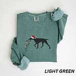 Light Green crewneck sweatshirt laid flat with rolled cuffs, embroidered with a black German shorthaired pointer in a Santa hat carrying a string of Christmas lights