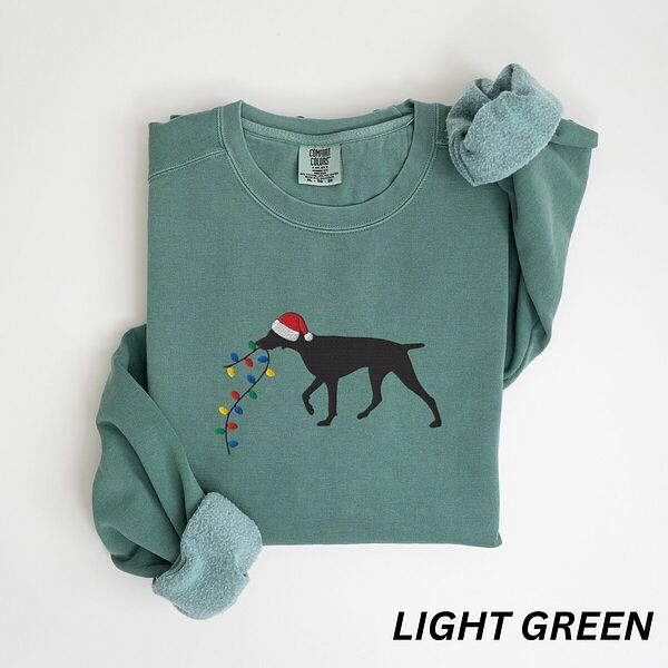 Light Green crewneck sweatshirt laid flat with rolled cuffs, embroidered with a black German shorthaired pointer in a Santa hat carrying a string of Christmas lights