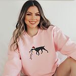 Woman in a Light Pink crewneck sweatshirt embroidered with a black German shorthaired pointer in a Santa hat carrying a string of Christmas lights