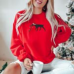 Woman by a Christmas tree in a Red crewneck sweatshirt embroidered with a black German shorthaired pointer in a Santa hat carrying a string of Christmas lights
