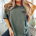 Woman in a Moss T-shirt embroidered with a black German shorthaired pointer in a Santa hat carrying a string of Christmas lights on the left chest