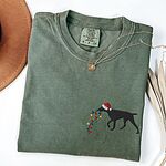 Moss T-shirt laid flat with a necklace, embroidered with a black German shorthaired pointer in a Santa hat carrying a string of Christmas lights on the left chest