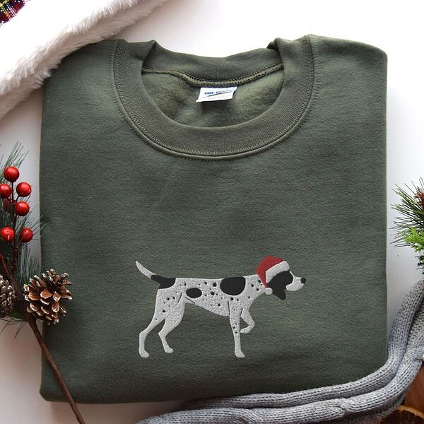Military Green crewneck sweatshirt laid flat with pine cones, red berries and a grey knit blanket, embroidered with a black and white ticked German shorthaired pointer in a red Santa hat