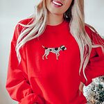 Woman by a Christmas tree in a Red crewneck sweatshirt embroidered with a black and white ticked German shorthaired pointer in a red Santa hat